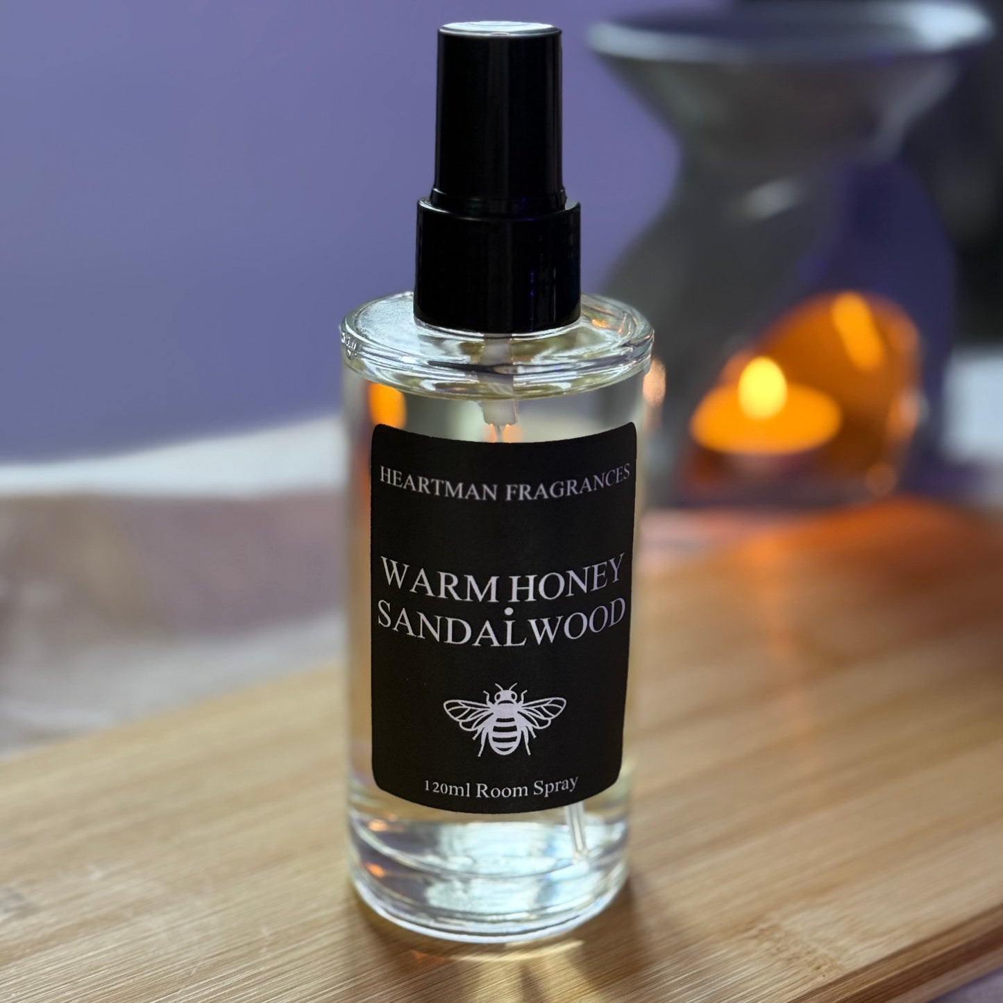 Bottle of Warm Honey Sandalwood room spray on a wooden surface with a blurred background