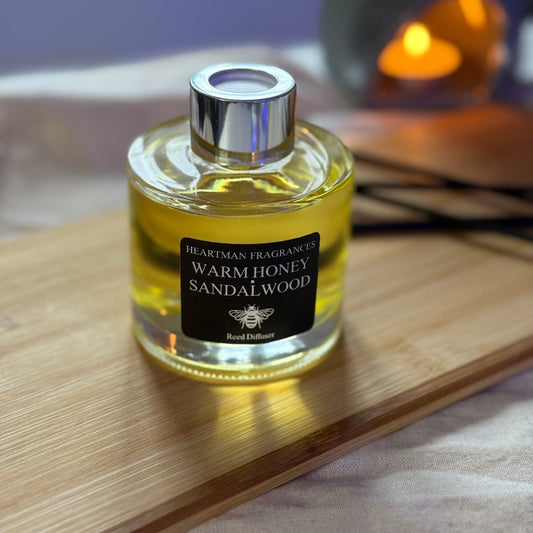 Bottle of Warm Honey Sandalwood fragrance on a wooden surface with a blurred candle in the background.
